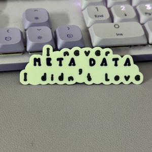 May include: A light green sticker with black text that reads "I never META DATA I didn't love". The sticker is placed on a purple keyboard.