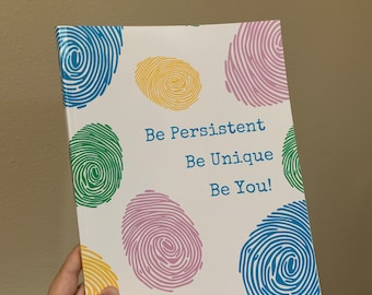 May include: A white booklet with a colorful fingerprint design and the text "Be Persistent Be Unique Be You!"