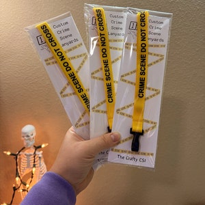 May include: Three yellow lanyards with black text that reads "Crime Scene Do Not Cross". The lanyards are packaged in clear plastic bags. The text "The Crafty CSI" is printed on the bottom of one of the bags.