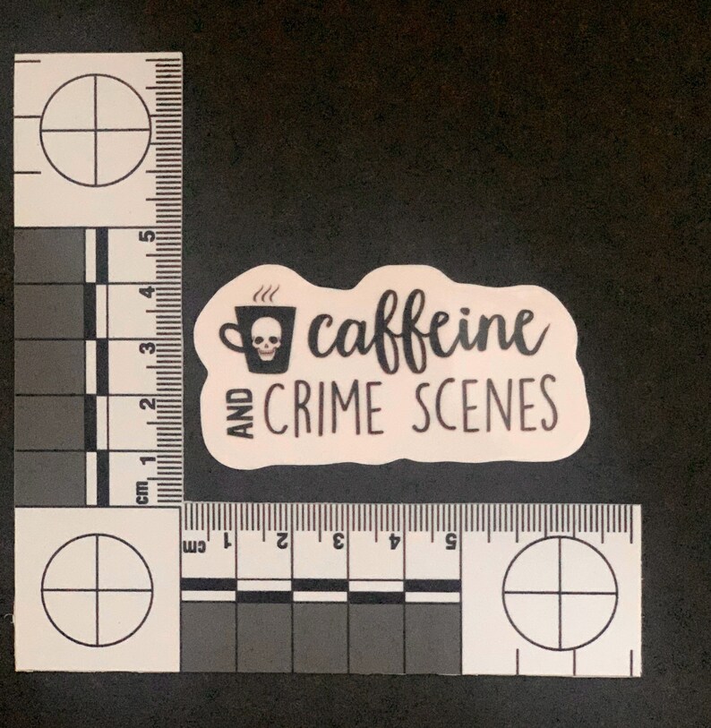 Puede incluir: Una pegatina rosa con texto negro que dice "caffeine and crime scenes". Una ilustraci&oacute;n en blanco y negro de una taza de caf&eacute; con una calavera en su interior est&aacute; por encima del texto.