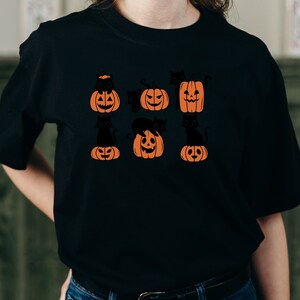 May include: Black t-shirt with a graphic of black cats sitting on orange pumpkins with jack-o'-lantern faces.