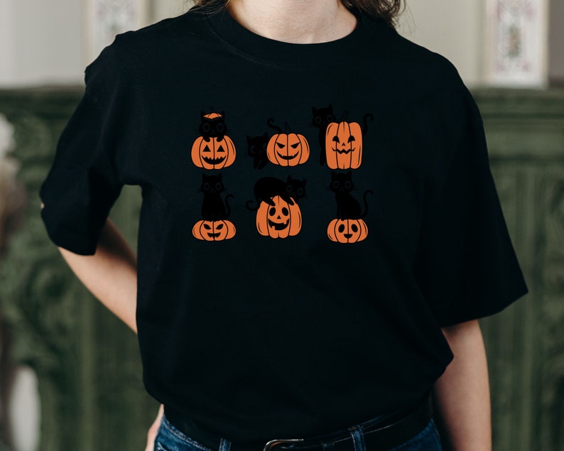 May include: Black t-shirt with a graphic of black cats sitting on orange pumpkins with jack-o'-lantern faces.