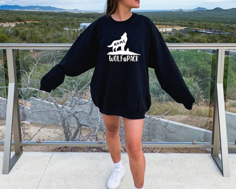 Pu&ograve; includere: Felpa nera con una silhouette di lupo bianca e il testo "NAME WOLF PACK".