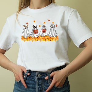May include: White t-shirt with a graphic of four dogs dressed as ghosts for Halloween. The dogs are walking in a line and are surrounded by orange and yellow fall leaves.