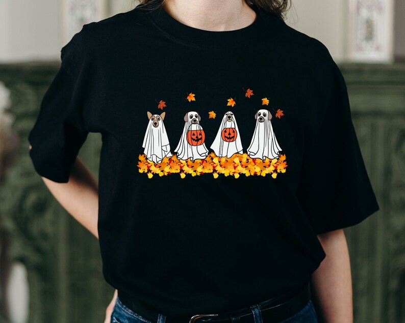 May include: Black t-shirt with a graphic of four dogs dressed as ghosts for Halloween. The dogs are holding pumpkins and are surrounded by autumn leaves.