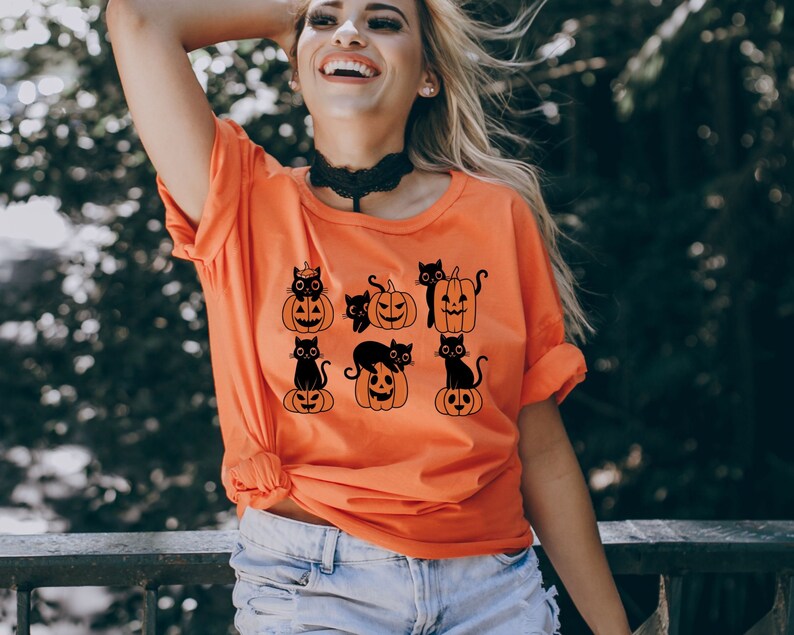 May include: Orange t-shirt with a black print of cats sitting on pumpkins. The cats are wearing witch hats and have spooky expressions.
