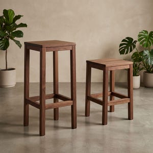 Puede incluir: Dos taburetes de bar de madera. El taburete más alto mide aproximadamente 76 cm de alto, y el taburete más bajo mide unos 51 cm de alto. Ambos taburetes tienen un asiento cuadrado y un diseño sencillo y robusto. La madera tiene un tono marrón cálido.