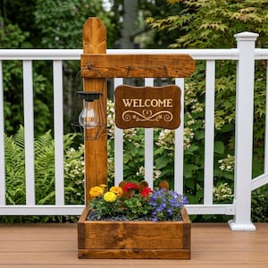 May include: A wooden welcome sign with a planter box filled with colorful flowers. The sign has a hanging lantern and the word "WELCOME" in white script. The planter box is filled with yellow, red, and blue flowers.