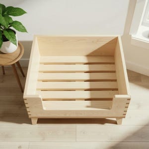 K&ouml;nnte beinhalten: Ein helles Haustierbett aus Holz mit Lattenrost und erh&ouml;hten Seiten. Das Bett hat eine rechteckige Form mit einem niedrigen Einstieg auf einer Seite und wird von kleinen Beinen getragen. Die Holzmaserung ist sichtbar.