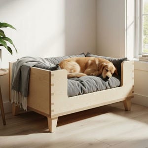Può includere: Un letto per cani in legno chiaro con un cuscino e cuscini grigi. Un golden retriever dorme sul letto, coperto da una coperta grigia. Il letto ha un design moderno con giunzioni visibili ed è posto in una stanza ben illuminata.