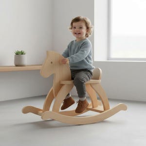 Puede incluir: Un balancín de madera de color claro, con un niño sentado en él. El caballo tiene un diseño sencillo con balancines curvos y un asiento. El niño lleva un jersey azul y pantalones grises.