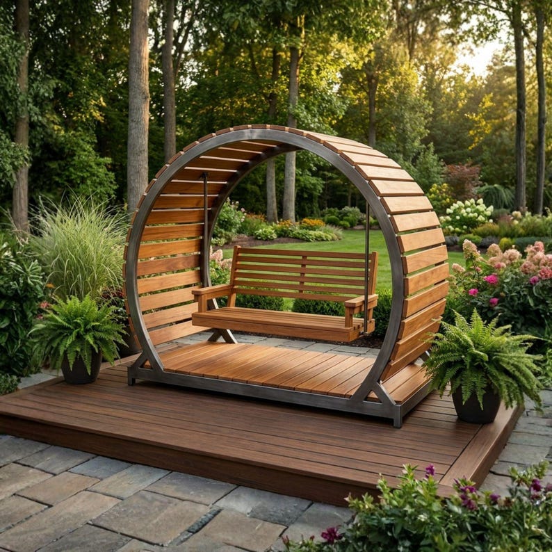 Puede incluir: Un columpio de madera con un marco circular y respaldo de listones de madera. El columpio tiene asiento y respaldo de listones. El marco es de metal y madera, sobre una plataforma de madera. El fondo es un jard&iacute;n.