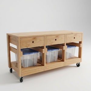 May include: A light-colored wooden storage unit with three drawers and three open compartments. Each compartment holds a clear plastic bin with a blue lid. The unit is on wheels for easy movement.