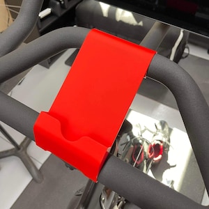 May include: A red plastic phone holder attached to the handlebars of a stationary exercise bike.