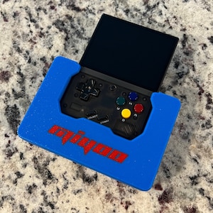 Op de afbeelding: Een blauwe case met het woord "Miyoo" in rood gedrukt, die een zwart draagbaar gameapparaat met een scherm, knoppen en een directionele pad bevat.