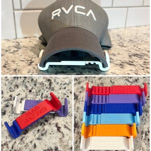 May include: A gray RVCA baseball cap is displayed with a white hat holder. Additional images show colorful plastic hat holders in red, blue, purple, orange, and white, each labeled "MAD HATTER".