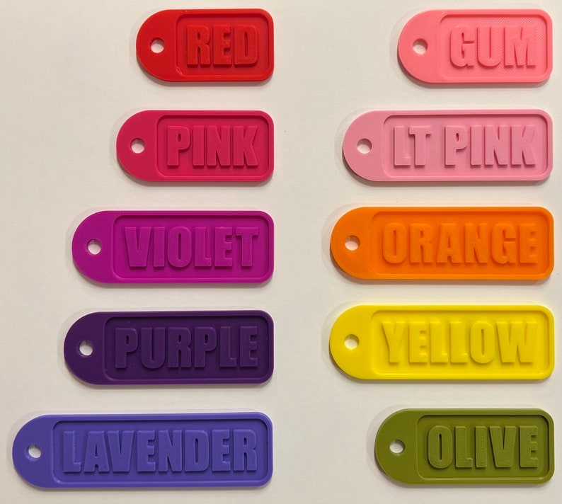 Op de afbeelding: Tien kleurrijke rechthoekige labels met afgeronde hoeken en een gat bovenaan. De labels zijn gelabeld met de volgende kleuren: Rood, Roze, Violet, Paars, Lavendel, Gom, Lichtroze, Oranje, Geel, Olijf.