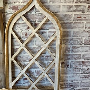 Puede incluir: Un marco de ventana decorativo de madera con un dise&ntilde;o de celos&iacute;a de diamantes. El marco tiene un acabado blanquecino desgastado con un borde de madera natural. El marco est&aacute; montado contra una pared de ladrillo envejecido.