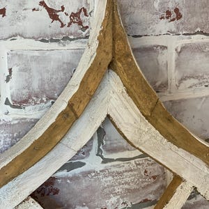 Puede incluir: Una pieza decorativa de arte mural de madera con un dise&ntilde;o en forma de diamante. El marco es de madera natural con detalles pintados de blanco, sobre un fondo de pared de ladrillo envejecido.