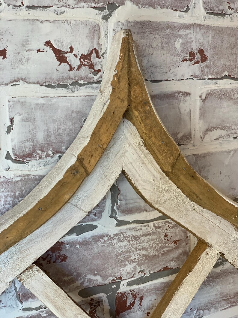Puede incluir: Una pieza decorativa de arte mural de madera con un dise&ntilde;o en forma de diamante. El marco es de madera natural con detalles pintados de blanco, sobre un fondo de pared de ladrillo envejecido.