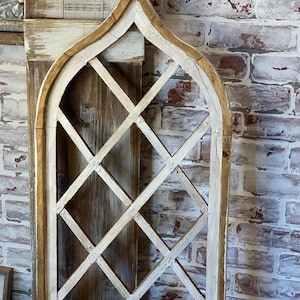 Puede incluir: Una decoraci&oacute;n de pared de madera envejecida con forma de ventana arqueada. El marco est&aacute; pintado de blanco con un borde de madera natural. El interior presenta un dise&ntilde;o de celos&iacute;a de diamantes. El fondo es una pared de ladrillo.