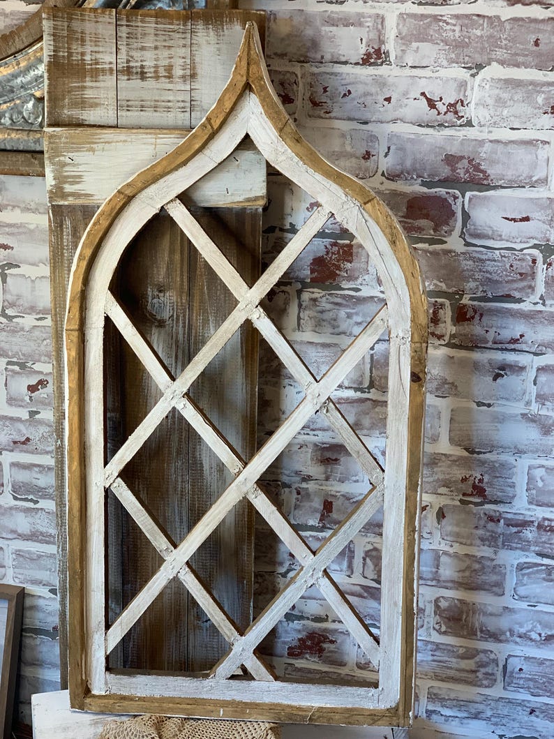 Puede incluir: Una decoraci&oacute;n de pared de madera envejecida con forma de ventana arqueada. El marco est&aacute; pintado de blanco con un borde de madera natural. El interior presenta un dise&ntilde;o de celos&iacute;a de diamantes. El fondo es una pared de ladrillo.
