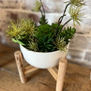 May include: A white ceramic planter with a wooden stand, filled with green succulents and dried flowers.
