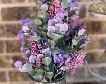 May include: A bouquet of purple and green eucalyptus stems in a clear glass vase. The stems have small purple flowers.