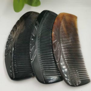 May include: Three handcrafted combs in shades of black and brown. Each comb has a curved shape, fine teeth, and a decorative leaf pattern carved into the handle. The combs are made of a glossy material.