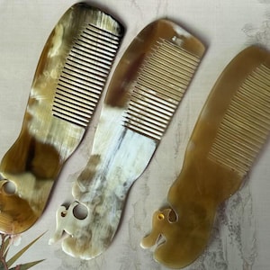 Puede incluir: Tres peines hechos a mano con un diseño único. Cada peine presenta un mango con forma de animal estilizado, con una combinación de colores marrón claro y crema. Los peines están hechos de un material natural.