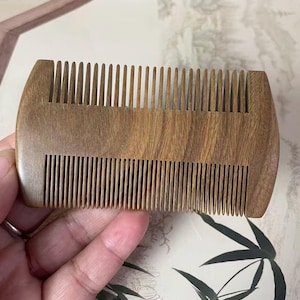 May include: A wooden comb with fine teeth. The comb is made of a light brown wood and has a smooth, polished finish. The comb has a rounded shape and is designed for grooming hair.