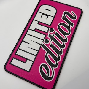 Op de afbeelding: Een rechthoekige sticker met een felroze achtergrond en een zwarte rand. De woorden "LIMITED" en "Edition" zijn in wit en zwart gedrukt. De tekst is vetgedrukt en zonder schreef.