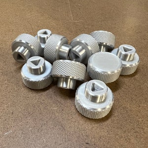 Könnte beinhalten: Eine Gruppe silberner Metallknöpfe mit einem dreieckigen Design auf der Oberseite. Die Knöpfe haben eine strukturierte Oberfläche und sind zu einem Stapel angeordnet.