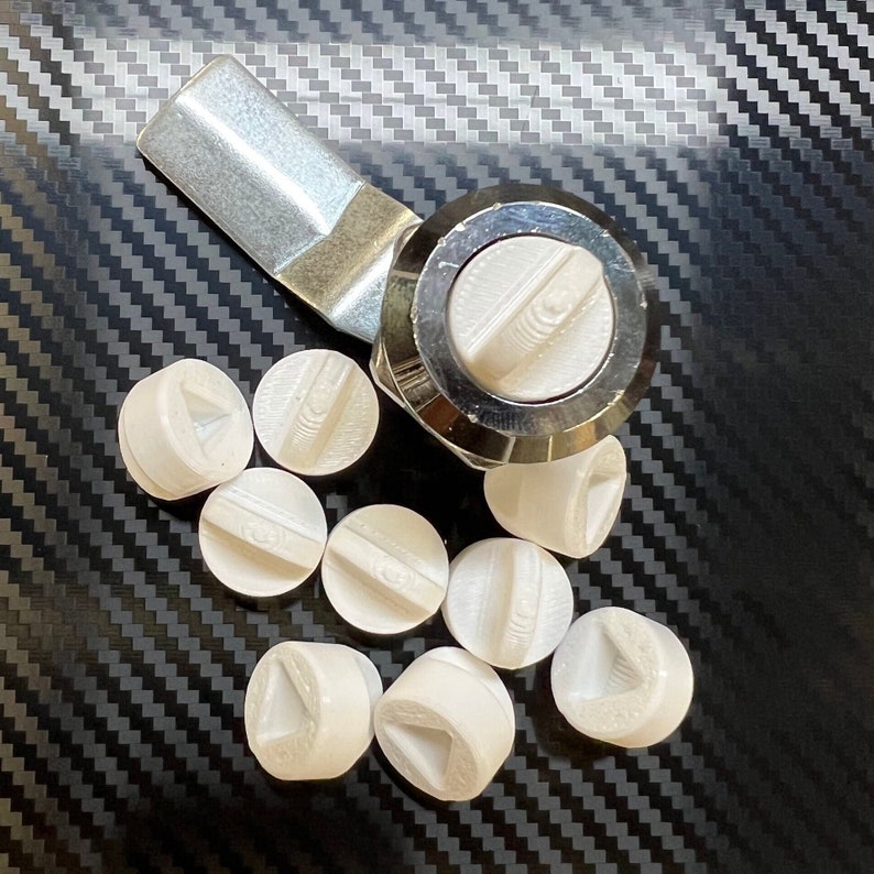 May include: A close-up of a silver and white cabinet knob with a round, white plastic handle. The knob is surrounded by ten white plastic knobs with various shapes and designs.