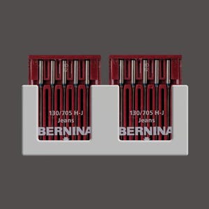 May include: Two white plastic holders with red and silver sewing needles. Each holder has the text "130/705 H-J Jeans BERNINA" printed on it.