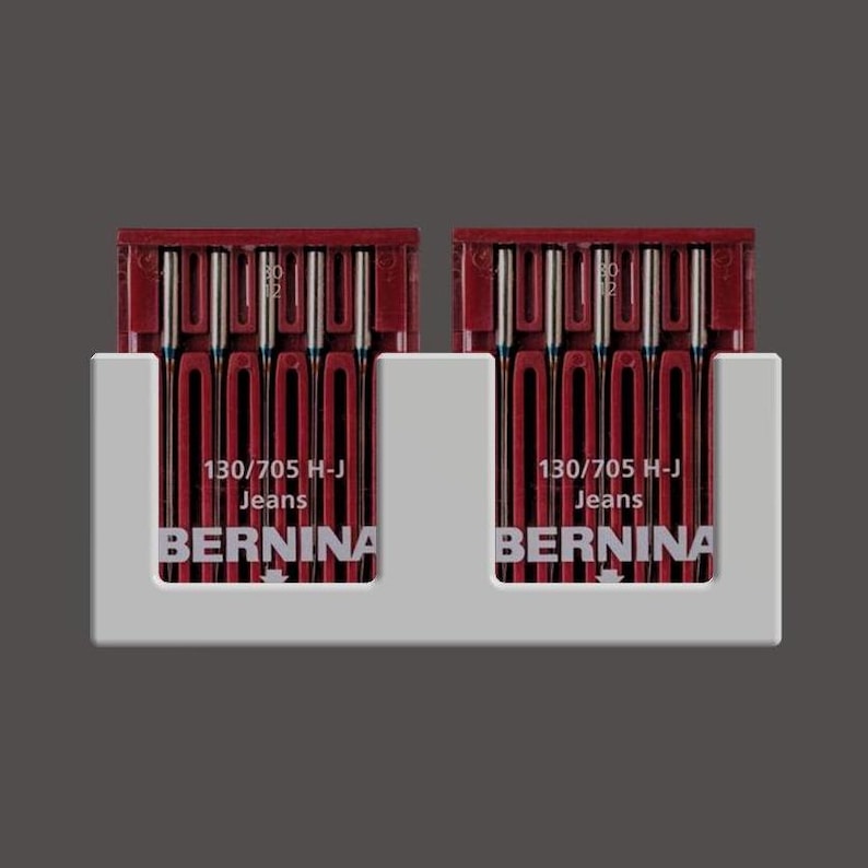 May include: Two white plastic holders with red and silver sewing needles. Each holder has the text "130/705 H-J Jeans BERNINA" printed on it.