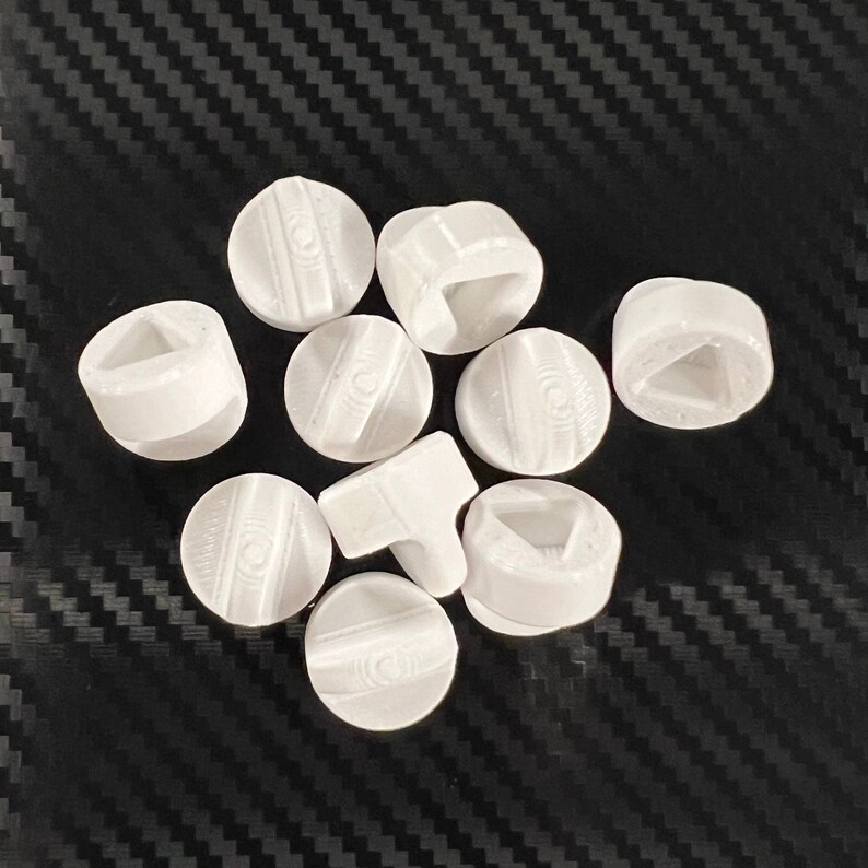 May include: A set of ten white plastic game pieces with different symbols on each side. The symbols include a triangle, a square, a circle, and a line.