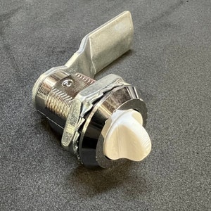 May include: A silver and white metal latch with a lever handle. The latch has a white plastic knob with a textured surface.