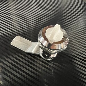 May include: A silver latch with a white plastic handle. The latch has a threaded barrel and a lever arm.