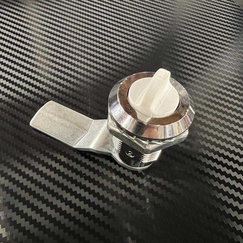 May include: A silver latch with a white plastic handle. The latch has a threaded barrel and a lever arm.