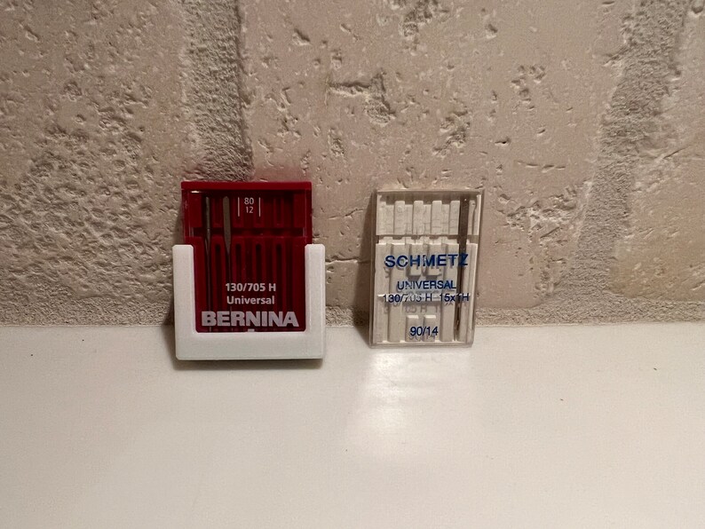 May include: Two packs of sewing machine needles. The pack on the left is red and white and says "130/705 H Universal BERNINA". The pack on the right is clear and white and says "SCHMETZ UNIVERSAL 130/705 H - 15x1H 90/14".