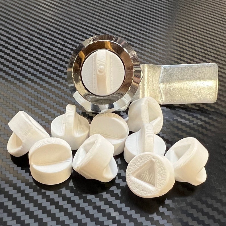 May include: A close-up of a silver door knob with a white plastic cover. The knob is surrounded by nine white plastic covers with different designs.