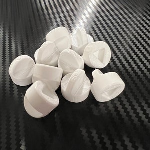 May include: A group of ten white plastic game pieces with different shapes and designs. The pieces are arranged in a pile on a black and white patterned surface.