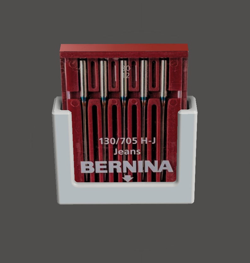 May include: A white plastic holder with a red plastic case of 10 sewing machine needles. The case has the text "130/705 H-J Jeans BERNINA" printed on it.