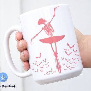 May include: White ceramic mug featuring a pink skeleton ballerina in a tutu, with bats flying around. The mug is held by a hand. The words "Instant Download" are at the bottom of the mug.
