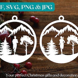 Puede incluir: Dos adornos navideños de silueta blanca que representan una escena de montaña con un corredor y árboles. Los adornos están sobre un fondo de madera.