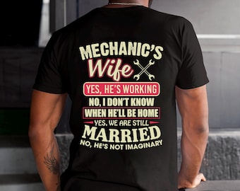 Puede incluir: Camiseta negra con el texto "MECHANIC'S Wife" y una llave inglesa cruzada. La camiseta incluye las frases "YES, HE'S WORKING", "YES, WE ARE STILL MARRIED" y "NO, HE'S NOT IMAGINARY".