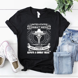 May include: Black t-shirt with a white graphic design that reads "United States Combat Medic" with a caduceus symbol and the text "Honor Duty Country Once a Combat Medic Always a Combat Medic".
