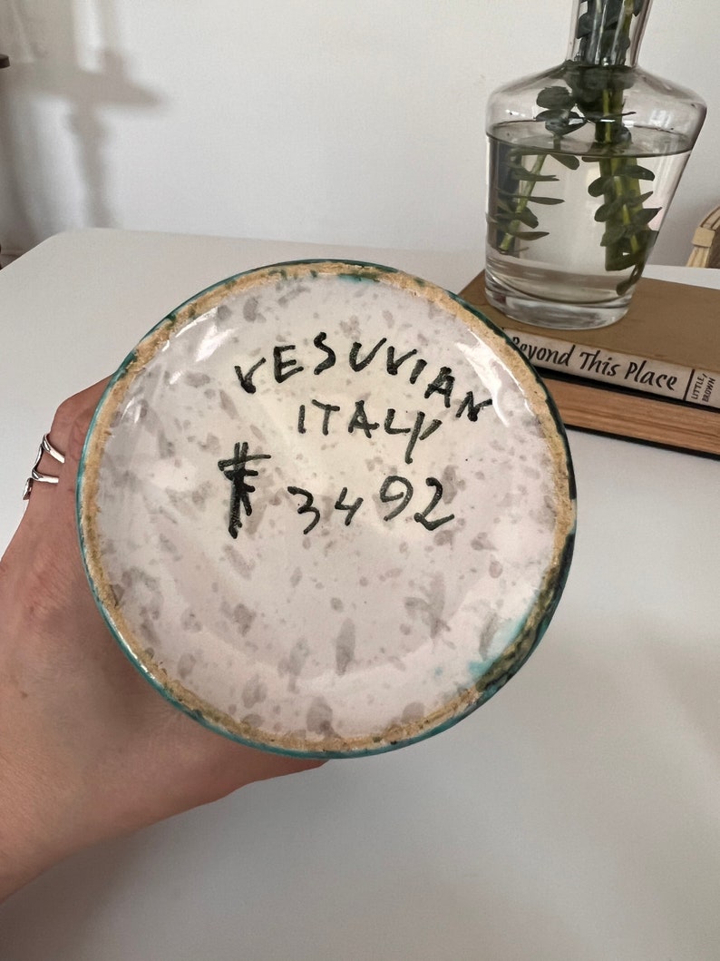 May include: A white ceramic vase with a green glaze and a handwritten inscription that reads "VESUVIAN ITALY # 34 92".