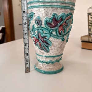 May include: A white ceramic vase with a turquoise glaze and raised floral design. The vase has a scalloped rim and base.